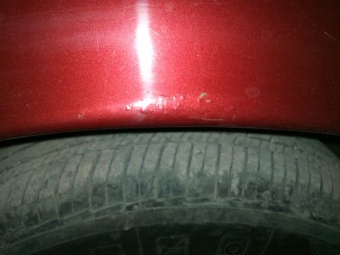 1998 Ford Crown Victoria - Close-up of a red car's fender showing damage and rust above a tire.
