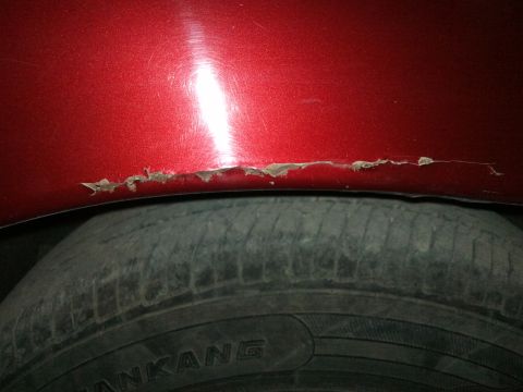 1998 Ford Crown Victoria - Peeling paint and rust damage on a red car fender above the tire. Website logo is visible.