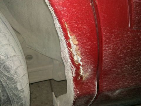 1998 Ford Crown Victoria - Rust is forming on the lower body panel near the rear tire of a vehicle.