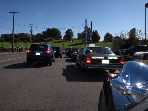 1991 Ford LTD Crown Victoria - black Highway Patrol sedan sits in a queue of cars on a road beside a green hillside on a sunny day.