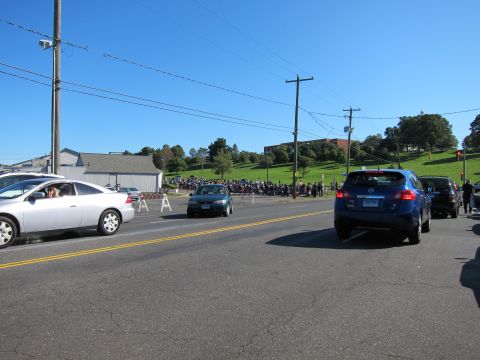 1991 Ford LTD Crown Victoria - Traffic on a two-lane road as a large crowd and rows of parked motorcycles gather on a grassy hill in the background.