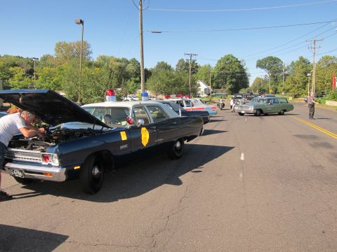 1991 Ford LTD Crown Victoria - vintage dark blue police sedan with state-patrol door emblem sits with its hood raised, ahead of more classic cars on the street.