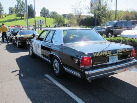 1991 Ford LTD Crown Victoria - Rear view of a black-and-white Ford LTD Crown Victoria Highway Patrol cruiser parked in a lot with other classic patrol cars.