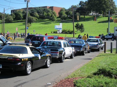 1991 Ford LTD Crown Victoria - line of vintage police cars curves along a road, led by a black Florida Highway Patrol cruiser and a black-and-white Police sedan.