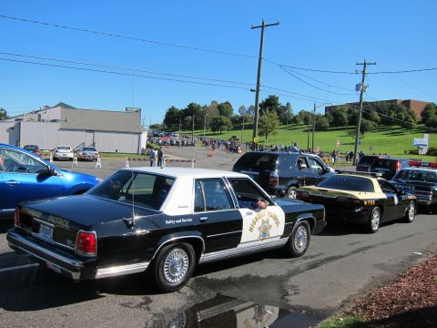 1991 Ford LTD Crown Victoria - black-and-white Ford Crown Victoria Highway Patrol car sits in a lot ahead of a yellow FHP cruiser, with a crowd on the hill behind.
