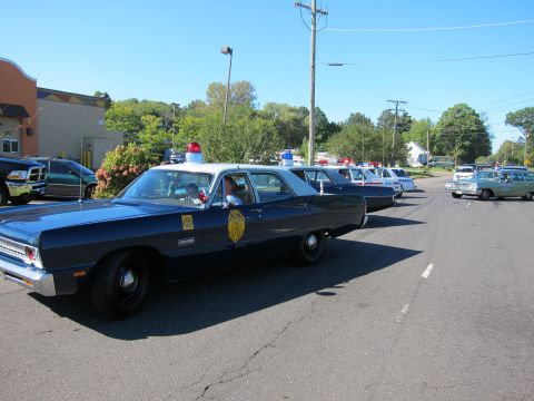 1991 Ford LTD Crown Victoria - dark blue vintage state police sedan with a single red roof light leads a line of classic patrol cars in a parking lot.