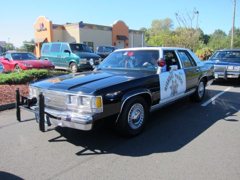 1991 Ford LTD Crown Victoria - black-and-white Ford LTD Crown Victoria Highway Patrol car with a front push bar parked in a lot before a Mexican restaurant.