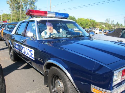 1991 Ford LTD Crown Victoria - blue and white classic POLICE sedan with light bar sits with a person inside, photographed close up at an outdoor gathering.