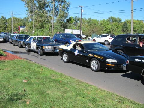 1991 Ford LTD Crown Victoria - black STATE TROOPER Camaro and other classic police cars are lined up along a curb in a parking area.