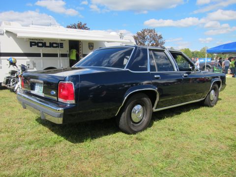 1991 Ford LTD Crown Victoria - dark blue Ford four-door sedan sits on grass at an outdoor show next to a MERIDEN POLICE command truck.