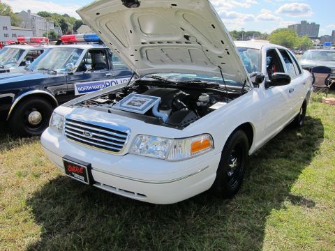 1991 Ford LTD Crown Victoria - white Ford Crown Victoria police car sits on grass with its hood raised showing the engine, beside other cruisers at a show.