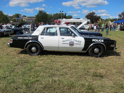 1991 Ford LTD Crown Victoria - Side profile of a black-and-white Jaffrey Police sedan marked Street Crime Unit, with roof light bar, parked on grass.