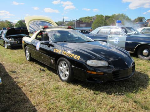 1991 Ford LTD Crown Victoria - black State Trooper coupe with gold lettering and open hood sits on grass beside other police cars at a show.