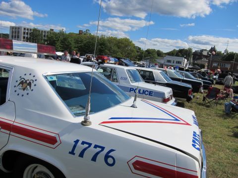 1991 Ford LTD Crown Victoria - Rear quarter view of a white State Police car numbered 1776 with eagle emblem, beside a line of parked patrol cars.