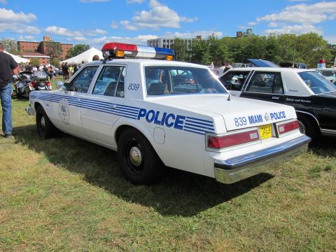 1991 Ford LTD Crown Victoria - Rear three-quarter view of a white Miami Police sedan numbered 839 with blue striping parked on grass at a show.