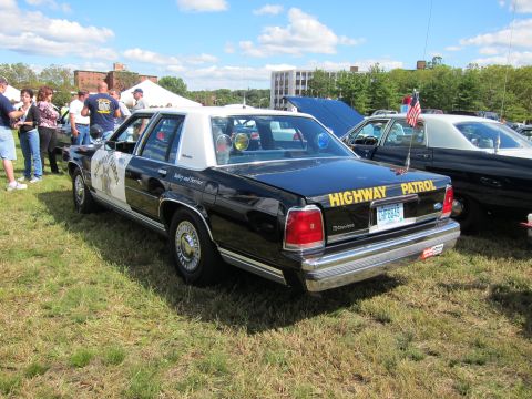 1991 Ford LTD Crown Victoria - Rear three-quarter view of a black-and-white Highway Patrol sedan with star emblem parked on grass at a car show.