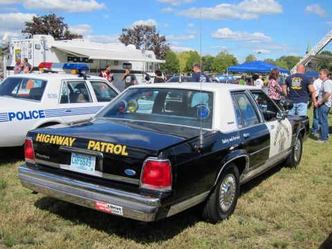 1991 Ford LTD Crown Victoria - Rear view of a black-and-white Highway Patrol sedan with a star door emblem parked on grass beside a white Police car.
