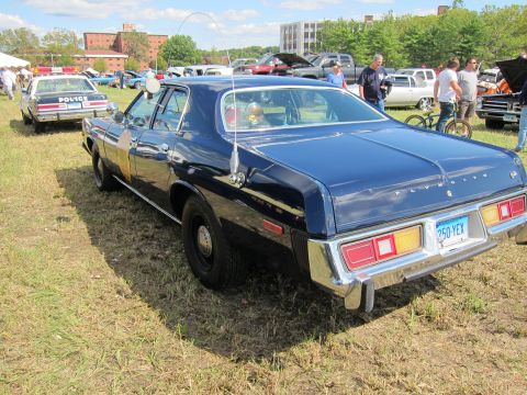 1991 Ford LTD Crown Victoria - dark blue Plymouth four-door police sedan is parked rear-facing on grass among other classic police cars at a show.