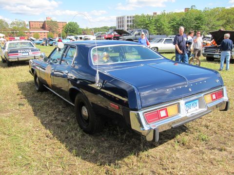 1991 Ford LTD Crown Victoria - dark blue Plymouth police sedan shown from the rear sits on grass with a row of classic cars and onlookers behind it.