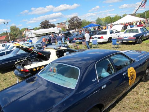 1991 Ford LTD Crown Victoria - Rows of classic police cars line a grassy field, including a dark blue sedan with a door emblem and a black coupe at a car show.