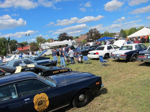 1991 Ford LTD Crown Victoria - Trumbull Police sedan and State Trooper-marked cruisers are lined up on grass with spectators and tents at an outdoor police car show.