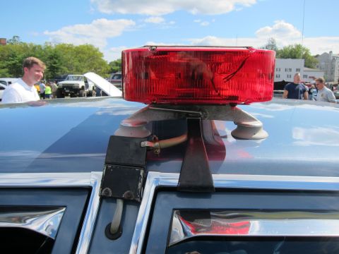 1991 Ford LTD Crown Victoria - close-up shows a single red rotating beacon light suction-mounted to the roof of a police car at an outdoor event.
