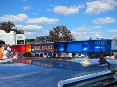 1991 Ford LTD Crown Victoria - State Police roof light bar with red and blue lenses is shown close-up, its lettering mirrored in the polished car roof.