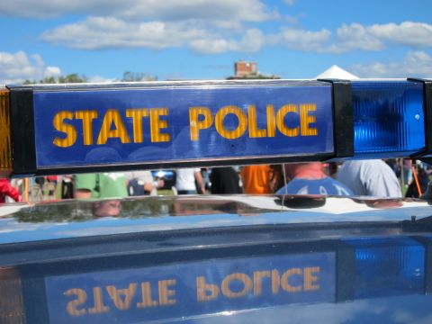 1991 Ford LTD Crown Victoria - close-up of a blue STATE POLICE light bar panel with gold lettering, reflected on the car roof, with a crowd in the background.
