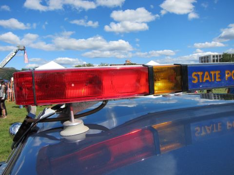 1991 Ford LTD Crown Victoria - close-up of the red and amber end of a STATE POLICE roof light bar, mounted on a car roof against a partly cloudy sky.