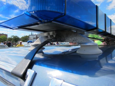 1991 Ford LTD Crown Victoria - low close-up shows a blue roof light bar suction-mounted to a police car roof, with people and buildings blurred behind.