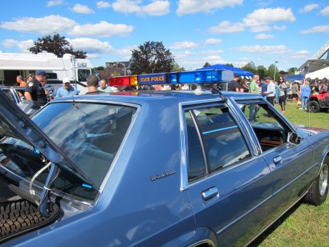 1991 Ford LTD Crown Victoria - blue Ford LTD Crown Victoria State Police sedan is shown from the side with a roof light bar, parked on grass at a car show.