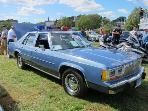 1991 Ford LTD Crown Victoria - light blue Ford LTD Crown Victoria State Police sedan with a roof light bar sits on grass at a show, with onlookers nearby.