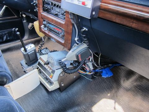 1991 Ford LTD Crown Victoria - interior floor area of a police car shows a mounted two-way radio with handset microphone, switches and bundled wiring.