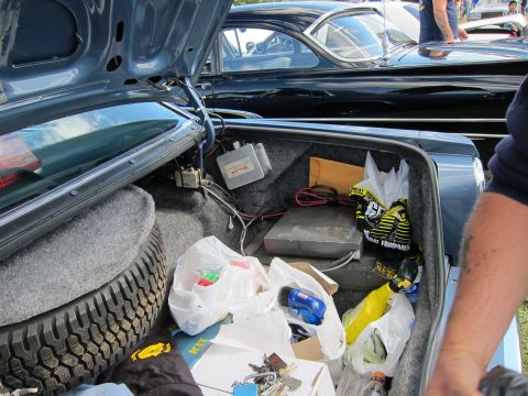 1991 Ford LTD Crown Victoria - Trunk of a classic show car opened to reveal a spare tire, gray electronic boxes, wiring, and several full plastic shopping bags.