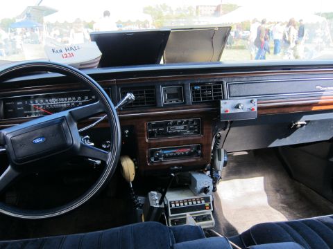 1991 Ford LTD Crown Victoria - Ford-badged steering wheel and woodgrain dashboard with an open glovebox, factory radio, and a center-mounted two-way radio control head.