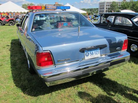 1991 Ford LTD Crown Victoria - Rear of a blue Ford LTD Crown Victoria police cruiser with a State Police roof lightbar and Connecticut plate, parked beside a black classi…