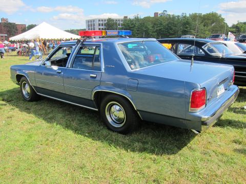 1991 Ford LTD Crown Victoria - Rear three-quarter view of a light blue Ford LTD Crown Victoria police sedan with a roof lightbar, displayed on a grassy car-show field.