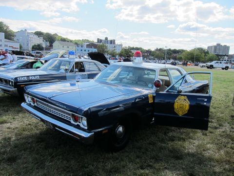 1991 Ford LTD Crown Victoria - Front three-quarter view of a dark blue Plymouth police sedan with a red roof beacon and gold State Police door shield, door open at a car…