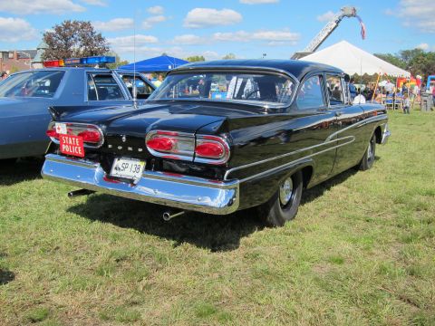 1991 Ford LTD Crown Victoria - Rear three-quarter view of a black classic Ford two-door sedan with round taillights and a red State Police plate above Massachusetts plate…