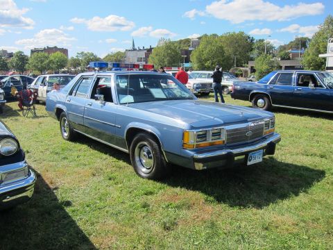 1991 Ford LTD Crown Victoria - light blue Ford LTD Crown Victoria sedan fitted with a roof lightbar sits on grass at an outdoor classic car show.
