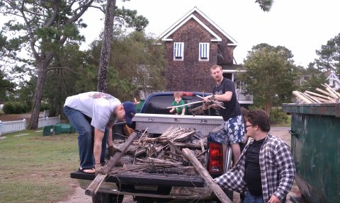 1979 Ford Bronco - People are loading wood debris into the bed of a pickup truck next to a dumpster.