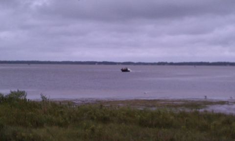 1979 Ford Bronco - A small boat travels across a calm bay under an overcast sky.