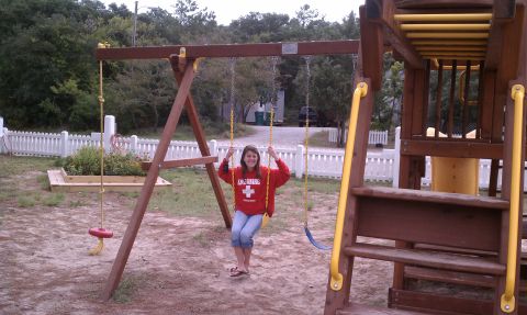 1979 Ford Bronco - A person enjoys a swing on a wooden playground set with a white picket fence in the background.