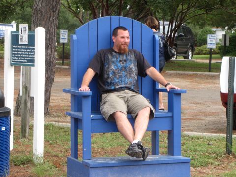 1979 Ford Bronco - A man relaxes in an oversized blue chair, with a dark SUV visible behind him.