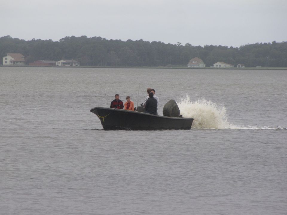 Dark boat with three people moving through water, creating a large wake