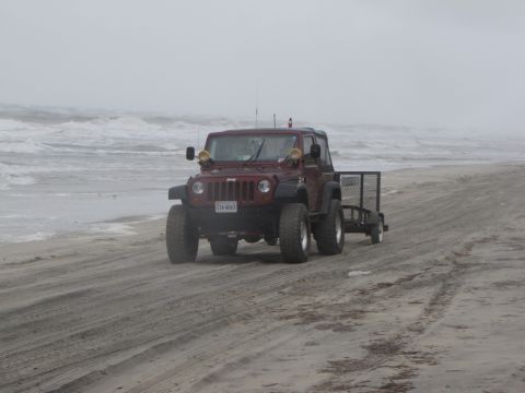 1979 Ford Bronco - Jeep Wrangler towing a trailer on the beach with the ocean nearby.