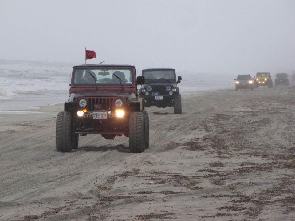 Red Jeep Wrangler driving on a sandy beach with a flag