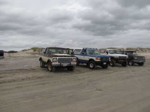 1979 Ford Bronco - Several 4x4 trucks and a Bronco are parked on the sand dunes on an overcast day.