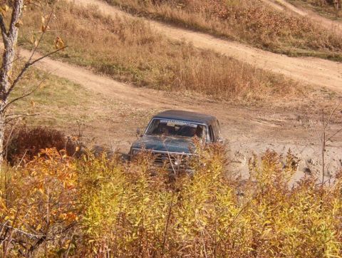 1986 Ford Bronco - A green 1986 Ford Bronco navigates a muddy dirt road surrounded by autumn foliage.