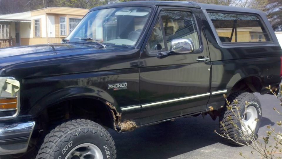 Black 1995 Ford Bronco with rust and large tires, 3/4 front view